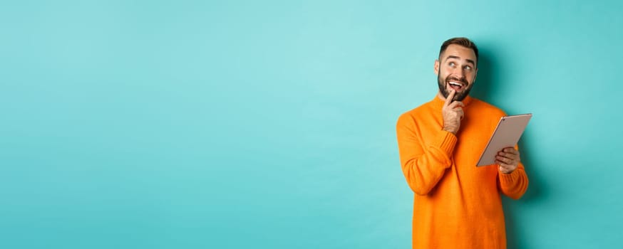 Handsome man thinking and using digital tablet, shopping online and pondering ideas, looking at upper left corner, standing over light blue background.