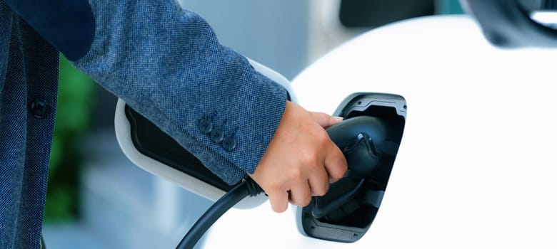 Progressive concept of hand insert an emission-free power connector to the battery of electric vehicle at home. Electric vehicle charging via cable from charging station to EV car battery