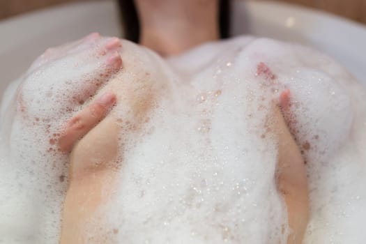 A sexy girl takes a bath. Large beautiful female breasts in bath foam.