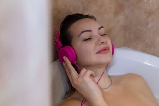 Beautiful young woman with headphones relaxing in bathtub.