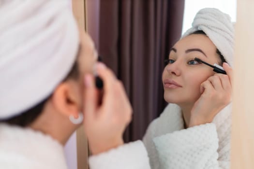 A woman applies black mascara to her eyelashes with a makeup brush. Young beautiful woman applying mascara makeup on her eyes in the bathroom.