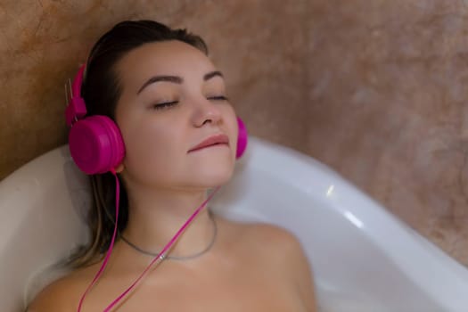 Beautiful young woman with headphones relaxing in bathtub.