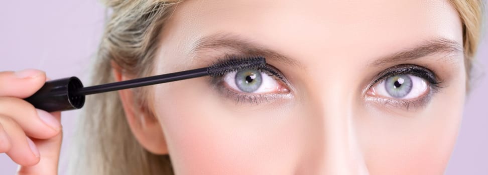 Closeup woman with blond hair putting alluring black mascara with brush in hand on long thick eyelash. Perfect fashionable cosmetic clean facial skin with beautiful eye young woman in high resolution.