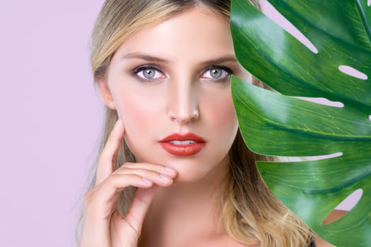 Closeup woman with perfect clean skin and alluring flawless natural soft facial makeup holding green leave monstera. Natural skincare treatment beauty or spa concept in pink isolated background.