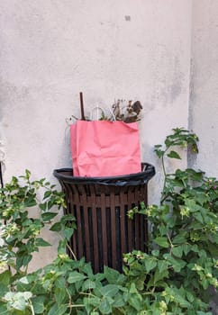 Luxury pink color bag in the trash bin on the street. France street luxury stylish paper bag with trash. Caring about nature, plastic pollution. High quality photo