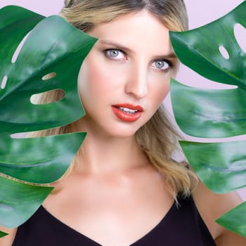 Closeup woman with perfect clean skin and alluring flawless natural soft facial makeup holding green leave monstera. Natural skincare treatment beauty or spa concept in pink isolated background.