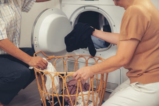 Senior couple working together to complete their household chores at the washing machine in a happy and contented manner. Husband and wife doing the usual tasks in the house.