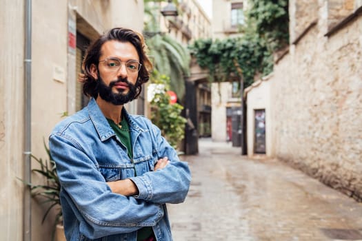 serious caucasian man with arms crossed in a nice old street with plants, concept of lifestyle and youth, copy space for text