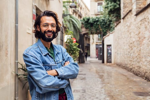 smiling caucasian man with arms crossed in a nice old street with plants, concept of lifestyle and youth, copy space for text