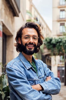 vertical portrait of a smiling caucasian man with arms crossed in a nice old street with plants, concept of lifestyle and youth, copy space for text
