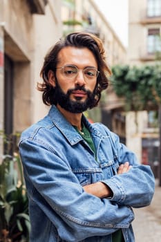 vertical portrait of a serious caucasian man with arms crossed in a nice old street with plants, concept of lifestyle and youth, copy space for text