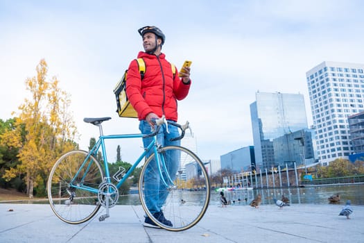 Food delivery concept. Young smiling African American driver with backpack looking smart phone in the city to deliver products for customers who order online purchases. Black male happy with his job.