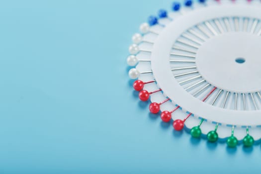 A set of multicolored needles pins in a round platform on a blue background with free space