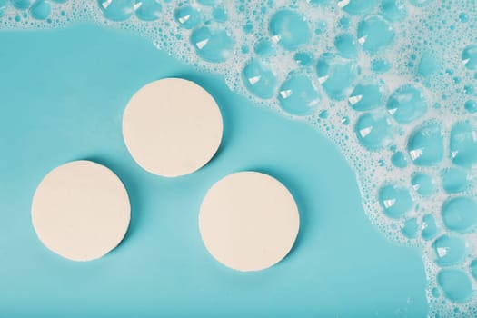 Three bars of round soap with foam on a blue background