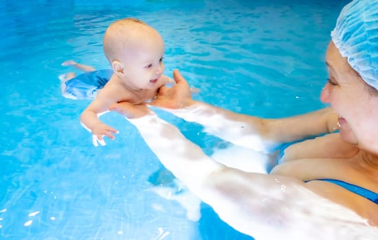 Adorable baby girl enjoying swimming in a pool with her mother early development class for infants teaching children to swim and dive. Swimming instructor doing exercises with a small child in the pool . High quality photo