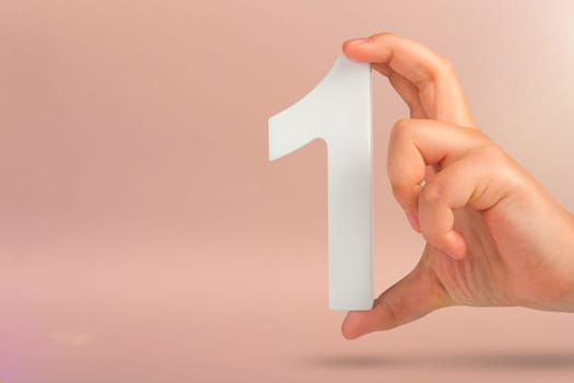 Number one in hand. A hand holds a white number one on a red background with copy space. Concept with number one. 1 percent rate, birthday, first or winner