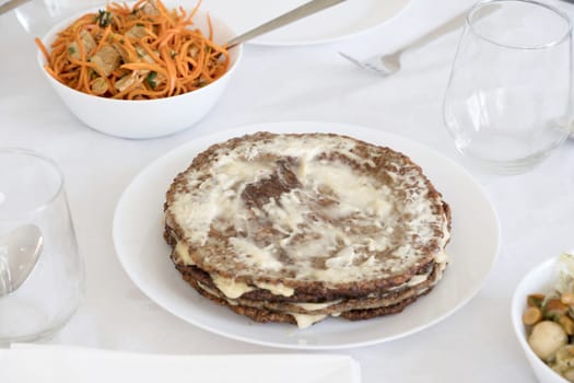traditional festive liver cake, pie with garlic and mayonnaise on the table for the holiday with Korean carrots in salad bowls, High quality photo