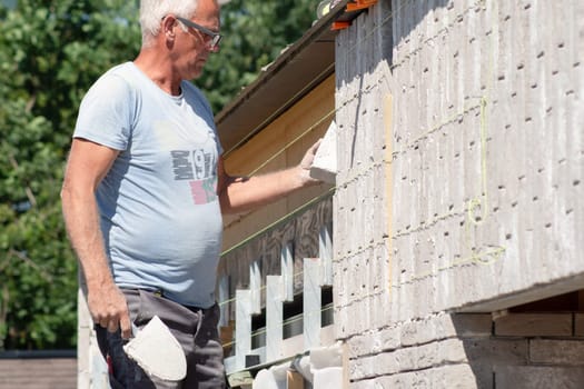 the bricklayer makes the facade of the house from gray bricks with cement and plaster at the construction site. High quality photo