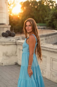 Woman sunset blue dress. Portrait of a woman with long hair and a blue dress against the backdrop of the setting sun and a white building. Lifestyle, walking around the city.