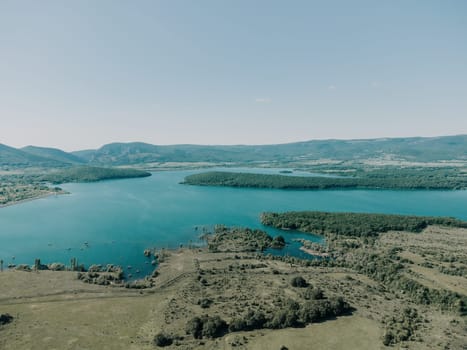 Aerial landscape from flying drone storage reservoir at mountain foot covered colorful spring forest. Beautiful view from above blue lake among highlands