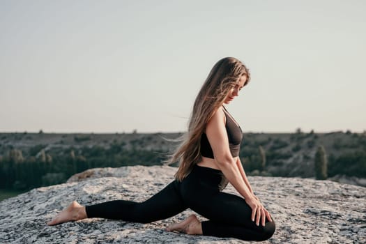 Well looking middle aged woman with long hair, fitness instructor in leggings and tops doing stretching and pilates on the rock near forest. Female fitness yoga routine concept. Healthy lifestyle.