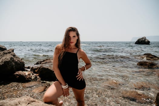 Woman travel sea. Young Happy woman in a long red dress posing on a beach near the sea on background of volcanic rocks, like in Iceland, sharing travel adventure journey