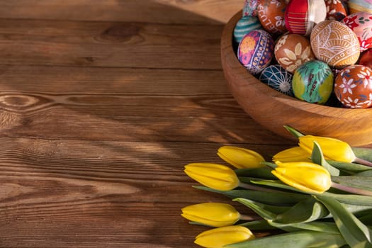 Hand-painted Easter eggs stacked on top of each other in a wooden bowl. Easter decoration as a base for your own composition or graphic inscriptions.