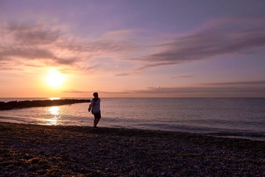 Boy playing pebble throwing on the beach at dawn. Unrecognisable, small pebble beach, sun, yellow and orange colours, life style