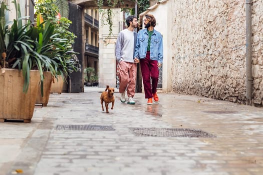 gay male couple walking with a little dog along a beautiful street, concept of leisure with pets and love between people of the same sex, copy space for text