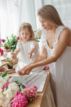 A little blonde girl with her mom on a kitchen countertop decorated with peonies. The concept of the relationship between mother and daughter. Spring atmosphere