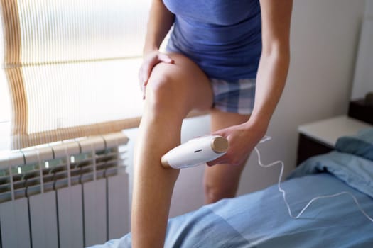 Anonymous female in sleepwear using pulsed light laser hair removal on leg while having beauty procedure at home