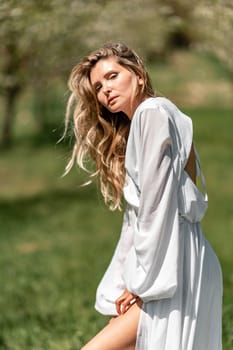 Blond blooming garden. A woman in a white dress walks through a blossoming cherry orchard. Long dress flies to the sides