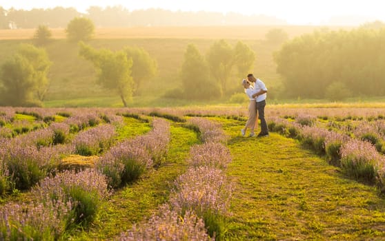 Smiling young couple embracing at the lavender field, holding hands, walking