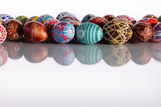 Composition of Easter eggs set in a row on a solid white background. The set Easter decoration is reflected in the glass.