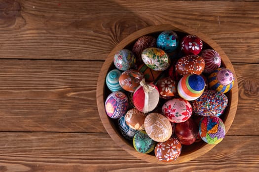 Top view of a wooden bowl filled with colorful Easter eggs. Easter composition with a view to adding graphic elements on your own.