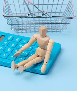 A wooden puppet and a blue calculator, behind a miniature shopping basket