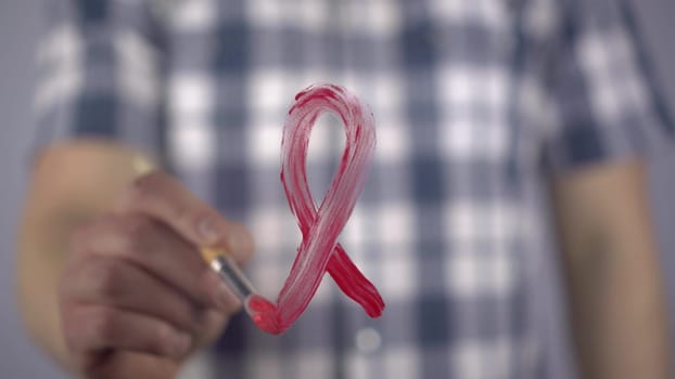 A young man paints with a brush the symbol of hiv in red. A man draws a red ribbon loop on the glass in support of cancer patients. Close-up. 4k