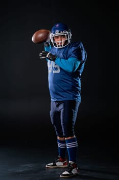 Portrait of a man in a blue uniform for american football throws the ball on a black background