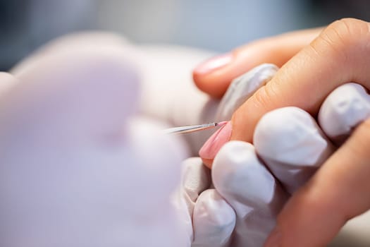 Blurred foreground. Large close-up on the hands of a beauty salon client. Performing a hybrid manicure in a professional beauty salon. Painting nails in pink.