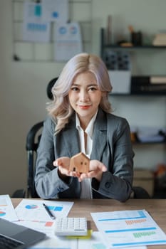 Accountant, businessman, real estate agent, Asian business man handing model house to customers along with house interest calculation documents for customers to sign.