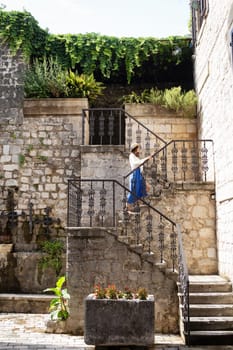 A girl in a blue dress and a straw hat walks the stairs in the old town of Kotor, Montenegro