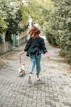 A girl and a boy are walking with a Jack Russell Terrier, walking down the street.