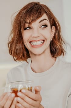 Woman drinks tea close-up. Portrait of a brunette in a white T-shirt with a transparent mug in her hands