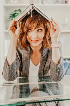 Woman book on her head. Surprised happy brunette in a jacket with a book on her head looks away against the backdrop of a bright office