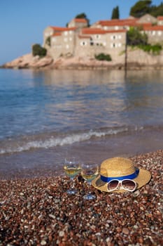 Sveti Stefan Island, Montenegro July 5, 2021: Adriatic Sea. A girl in a straw hat sits on the beach against the backdrop of St. Stephen's Island