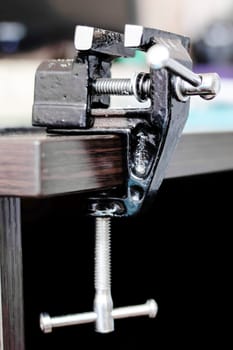 Black metal vise on the edge of a wooden table close up