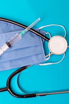 Two blue cotton medical masks, stethoscope and syringe on blue background close up