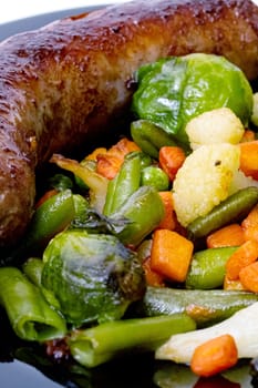 Grilled vegetables and sausage on a black plate close up