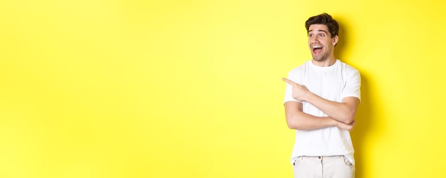 Excited smiling man pointing and looking left, checking out promo offer, standing over yellow background.