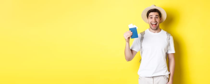 Tourism and vacation. Happy man tourist showing his passport with tickets, going on journey, standing over yellow background with backpack.